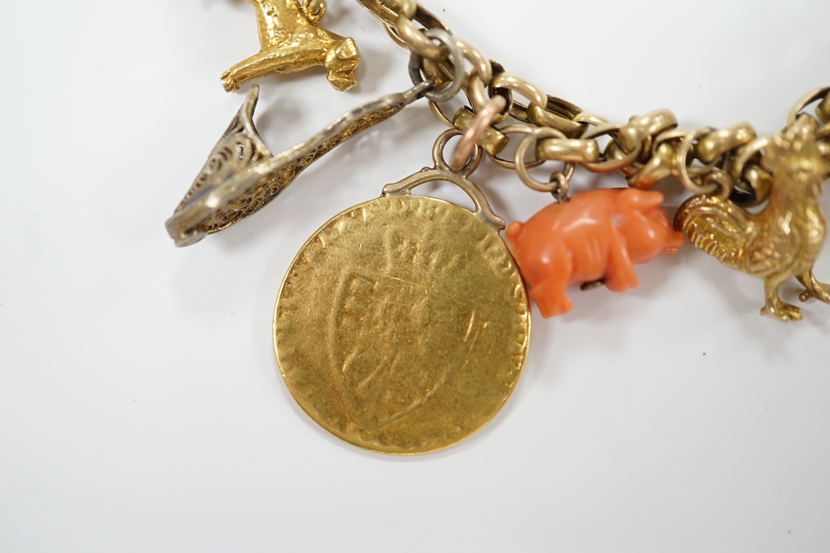 An early 20th century 9ct multi link charm bracelet, hung with sixteen assorted charms, including 9ct, coral, enamelled and a worn spade guinea